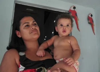 Mulher segurando bebê no colo em ambiente interno com papagaios vermelhos decorativos na parede azul