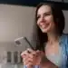 Mulher sorrindo enquanto segura o celular, simbolizando uma mensagem de alegria e otimismo para amigos.