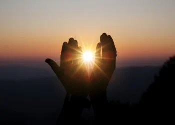 Mãos segurando o sol ao amanhecer, simbolizando fé, esperança e o início de um novo dia com Deus.