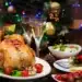 Prato de frango assado com legumes, decorado para o Natal, acompanhado de taças de vinho e uma decoração festiva ao fundo.