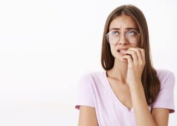 Mulher jovem com óculos, mordendo a unha e demonstrando ansiedade ou estresse, ilustrando o problema do apetite emocional e descontrole alimentar.