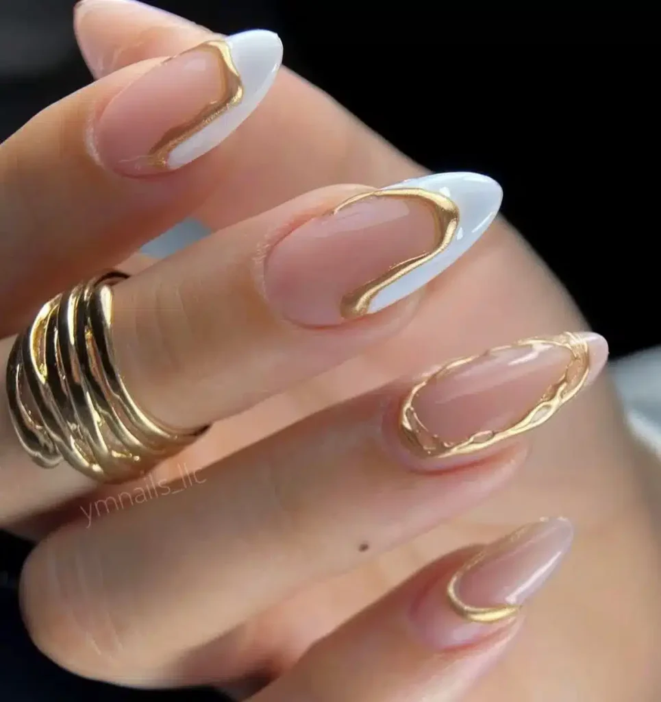 Unhas nude com detalhes dourados e toque de esmalte branco, estilo elegante e moderno.
