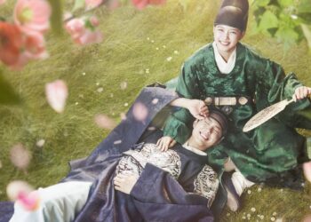 Casal de protagonistas do dorama Love in the Moonlight sorrindo em um campo de flores; a mulher veste trajes verdes de eunuco e o homem trajes reais azuis.