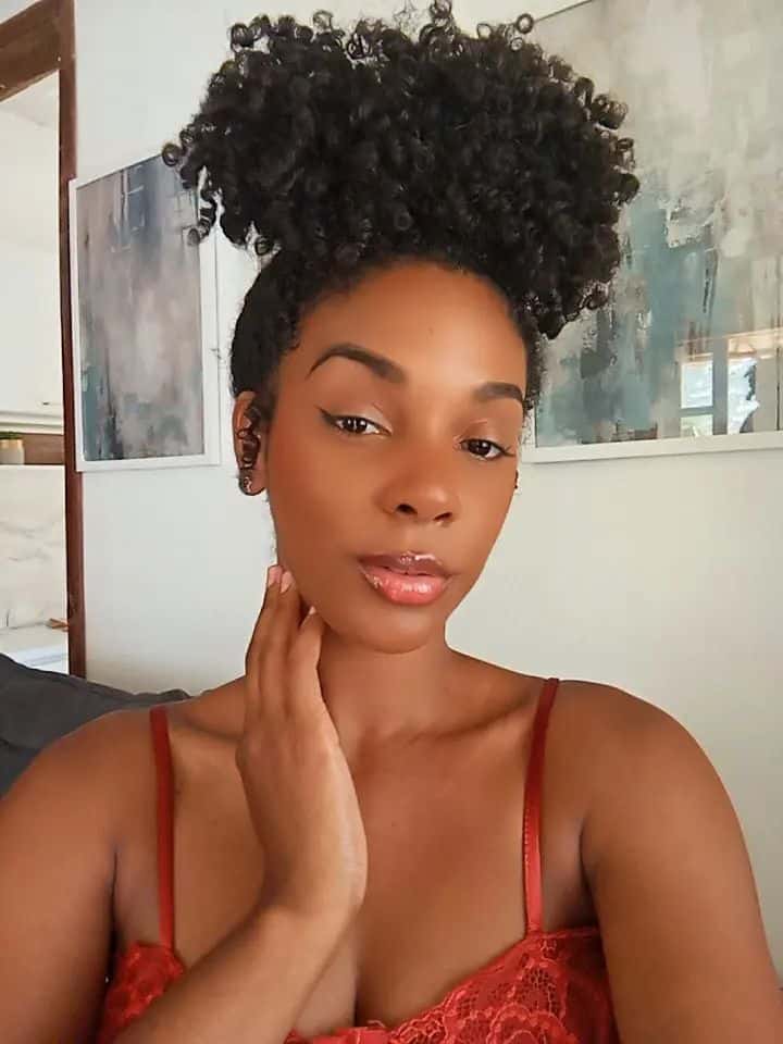 Mulher com cabelo crespo/cacheado escuro utilizando o penteado coque abacaxi de alto volume. O look é elegante, valorizando a textura natural do cabelo e a beleza dos cachos.