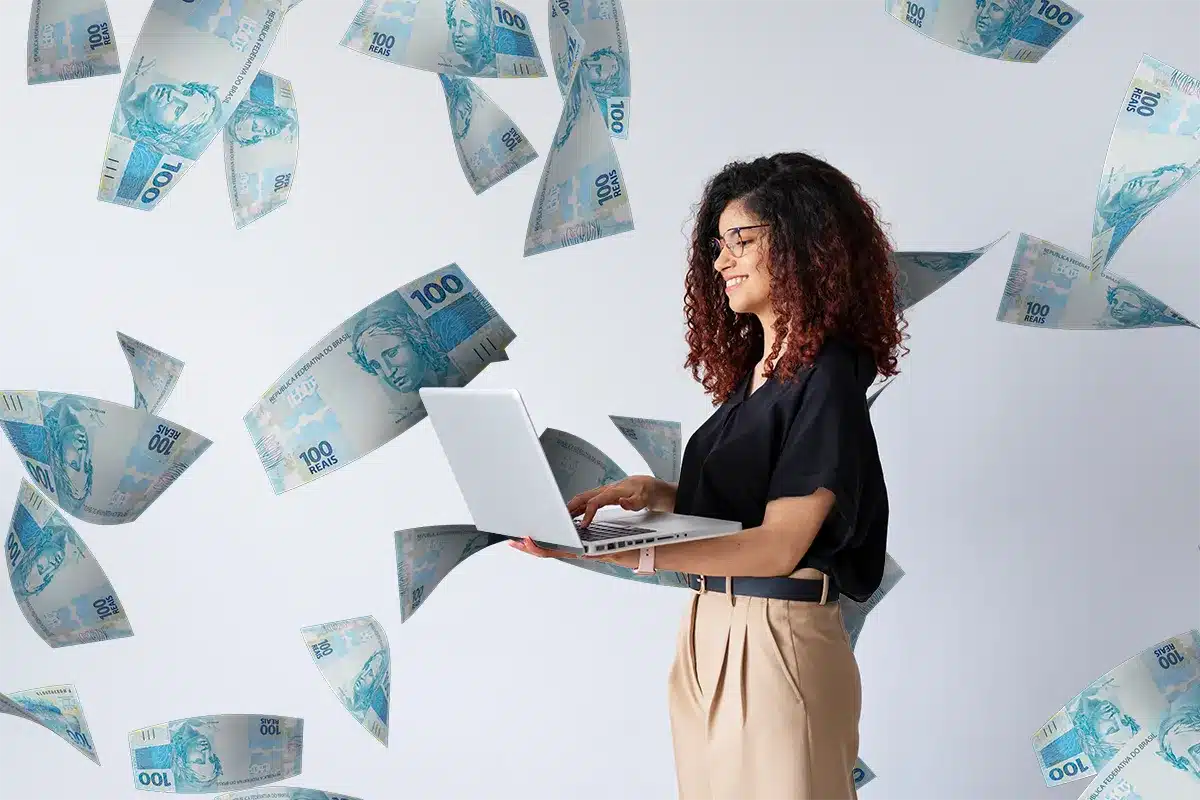 Mulher sorrindo usando laptop com notas de cem reais voando ao redor em fundo claro