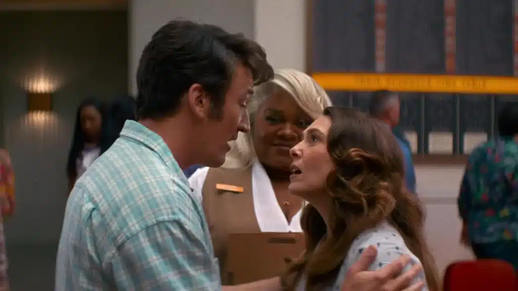 Cena do filme 'Eternidade', com um casal discutindo intensamente enquanto uma mulher observa ao fundo, em um ambiente interno.