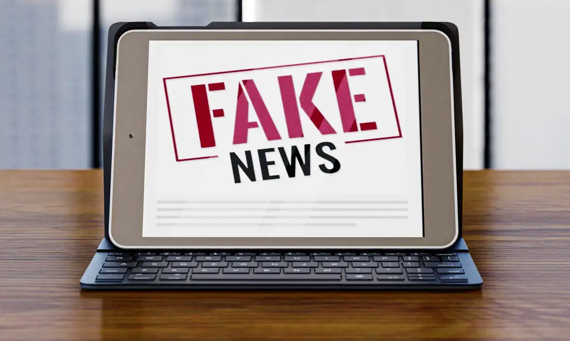 Tablet com a expressão FAKE NEWS exibida em vermelho e preto sobre mesa de madeira