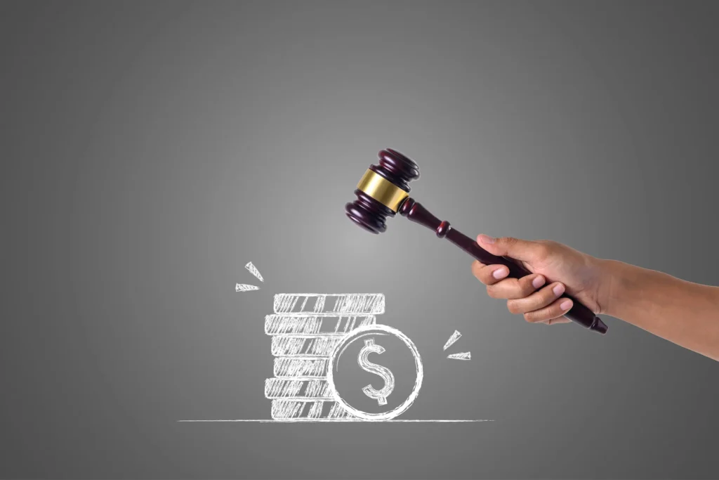 Mão segurando martelo de leilão sobre desenho de moedas, ilustrando passo a passo para participar do leilão eletrônico da Receita.