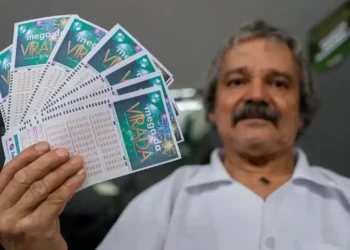 Homem segurando bilhetes da Mega da Virada, alertando sobre sites falsos que se passam pelas loterias da Caixa.