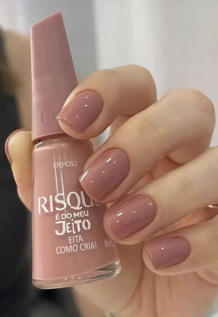 Esmalte nude rosado aplicado nas unhas, com acabamento cremoso e brilho suave.