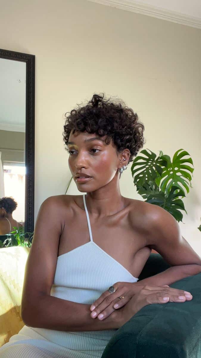 Mulher com corte de cabelo pixie cacheado, evidenciando volume no topo, textura definida e laterais curtas.