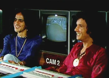 Caetano Veloso e Roberto Carlos sorrindo juntos durante uma gravação de TV, com uma tela de monitor ao fundo, simbolizando a amizade entre eles.