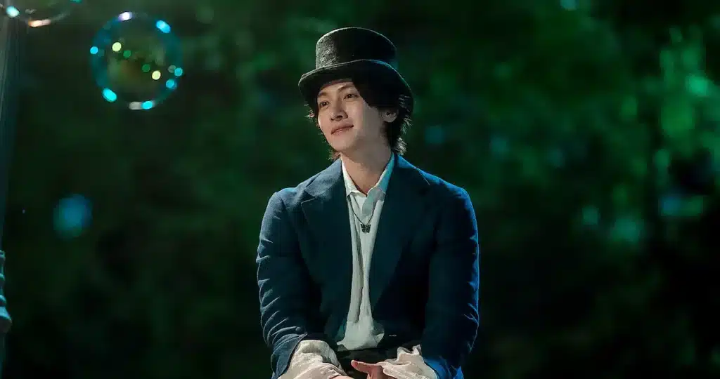 Homem misterioso sentado em um parque de diversões, com uma expressão tranquila e cercado por bolhas, em uma cena de The Sound of Magic.