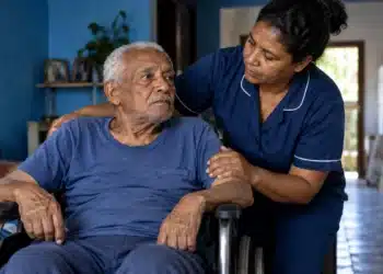 Idoso em cadeira de rodas recebe assistência de cuidadora em casa, ilustrando o adicional de 25% do INSS para aposentados por incapacidade.