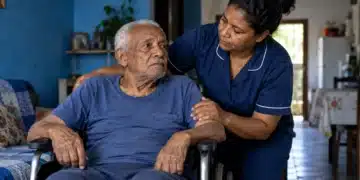 Idoso em cadeira de rodas recebe assistência de cuidadora em casa, ilustrando o adicional de 25% do INSS para aposentados por incapacidade.