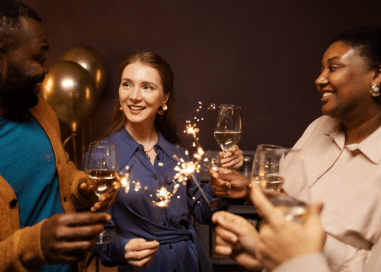 Grupo de amigos felizes brindando com taças de vinho branco e segurando fogos de artifício.