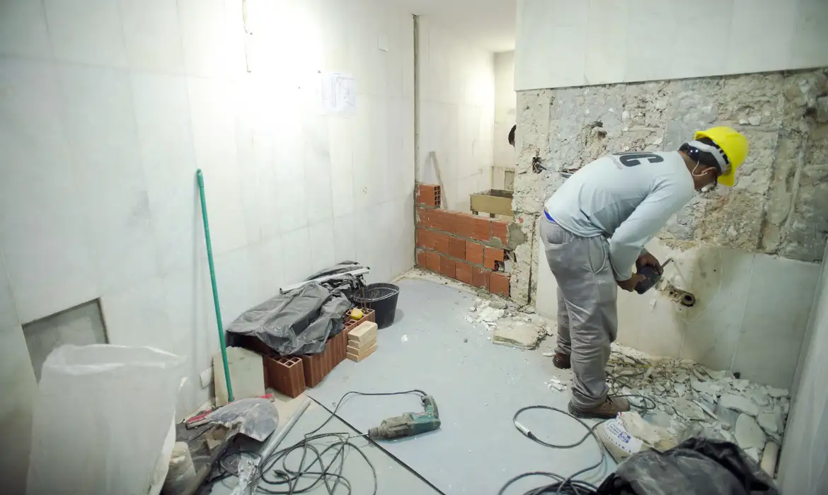 Trabalhador com capacete amarelo realizando demolição em parede interna de reforma residencial
