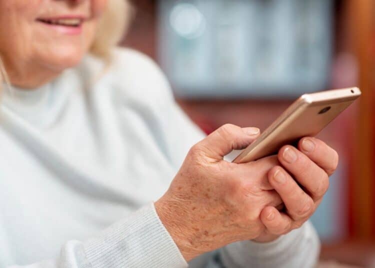 Close-up de uma pessoa mais velha sorrindo, digitando e enviando mensagens de bom domingo ou desejos de fim de semana pelo celular.