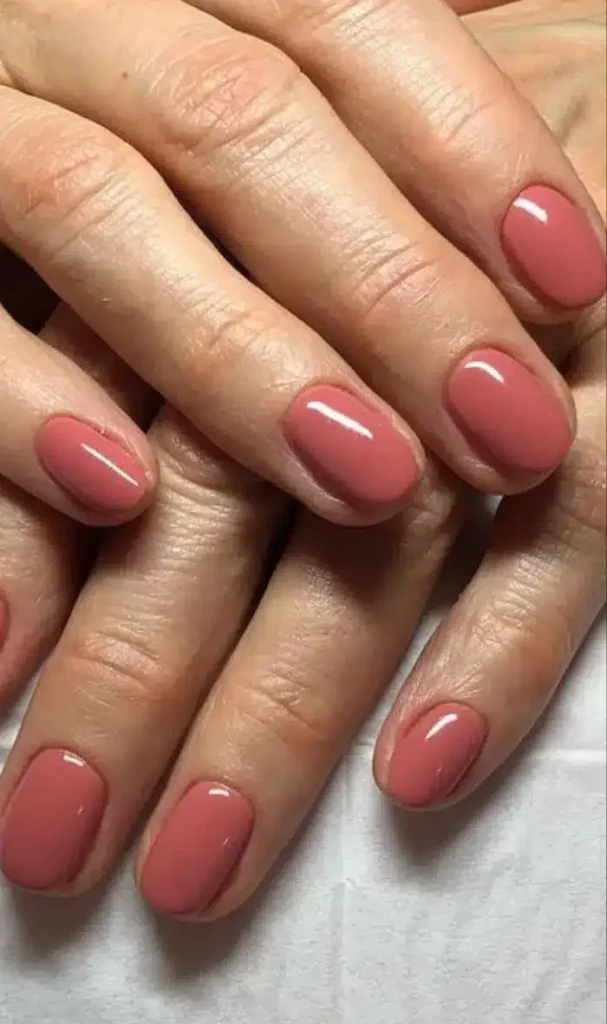 Unhas esmaltadas em tom coral suave com acabamento brilhante.