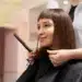 Mulher sorrindo enquanto faz o corte de cabelo no salão, com cabelo liso e franja.