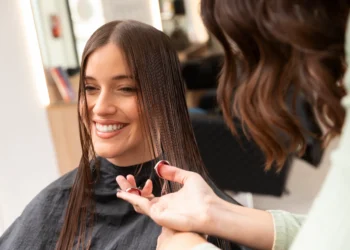 Mulher sorrindo enquanto recebe corte de cabelo reto e moderno no salão, com fios longos e repartidos ao meio.
