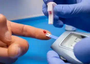 Pessoa realizando teste de glicemia com gota de sangue no dedo, ilustrando sintomas de diabetes que podem aparecer na boca.