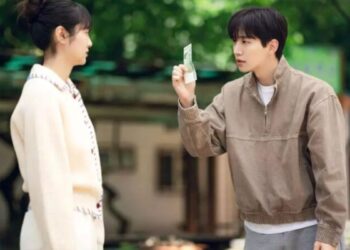 Cena de Cashero, com o protagonista mostrando uma nota de dinheiro para a personagem feminina, em um cenário ao ar livre.