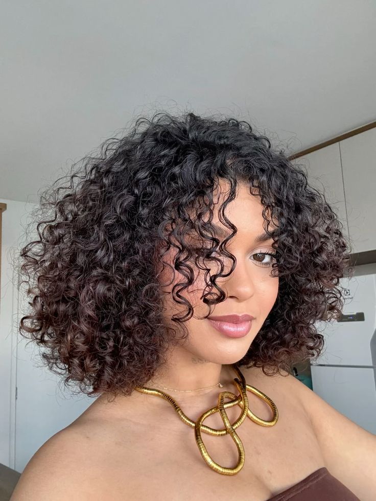 Mulher com cabelo cacheado volumoso em um corte arredondado (Rounded Cut) que realça o formato do rosto.