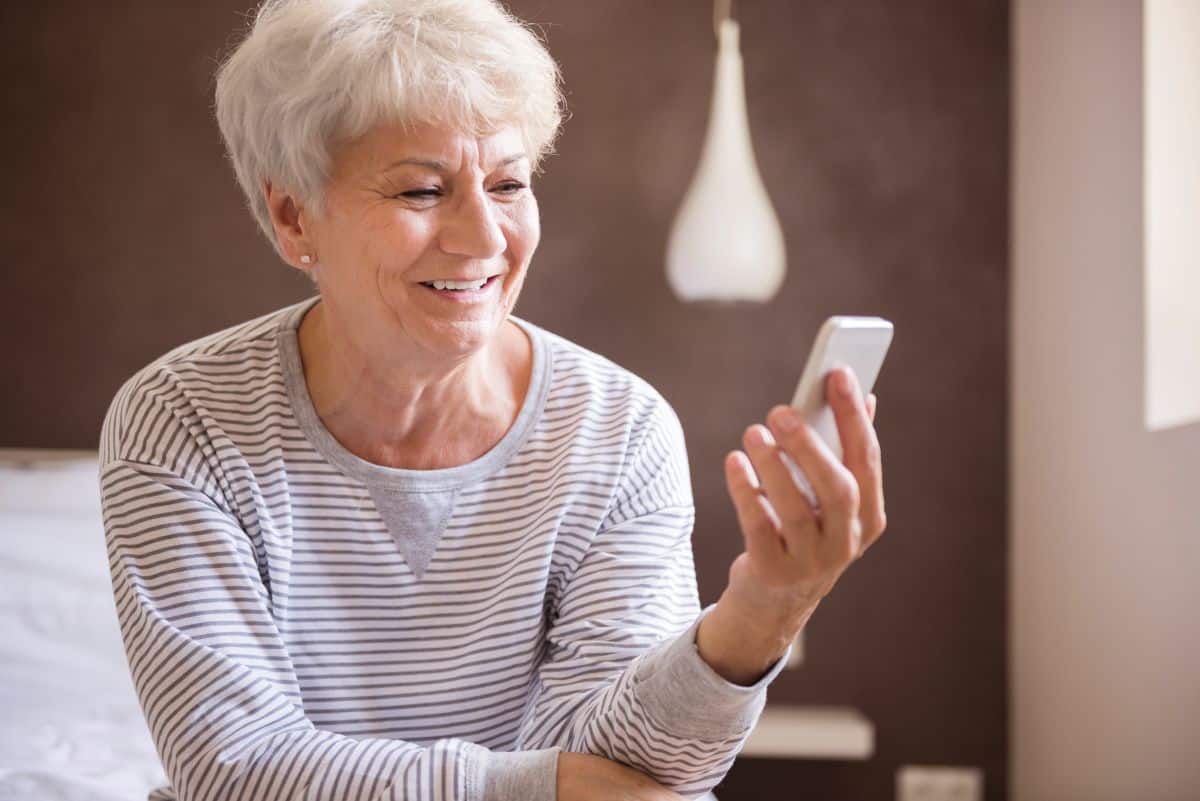 Mãos de uma mulher mais velha digitando uma mensagem de carinho no smartphone dourado, ilustrando a ação de enviar uma mensagem personalizada e especial para amigos.