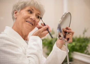Mulher aplicando maquiagem com pincel, realçando sua beleza e rejuvenescendo a aparência.