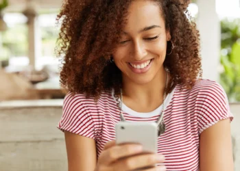 Pessoa sorrindo enquanto lê mensagem no celular, representando um momento carinhoso de bom dia.