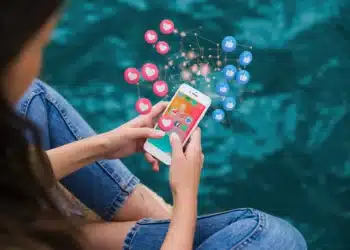 Pessoa usando celular com ícones de curtidas e reações representando mensagens inspiradoras de terça-feira para status nas redes sociais.