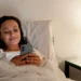 Mulher sorrindo na cama enquanto envia uma mensagem no celular, preparando-se para descansar após um dia cansativo de segunda-feira.