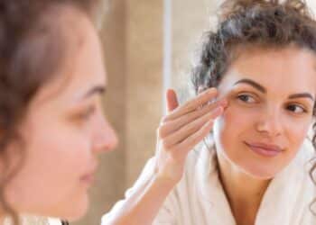 Mulher jovem com pele radiante apontando para a área dos olhos, demonstrando firmeza e hidratação na pálpebra inferior.