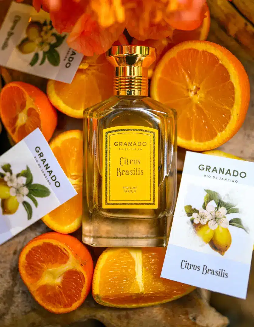 Frasco de perfume Granado Citrus Brasilis rodeado por laranjas e flores cítricas, ilustrando a explosão de notas cítricas e o toque floral da fragrância.