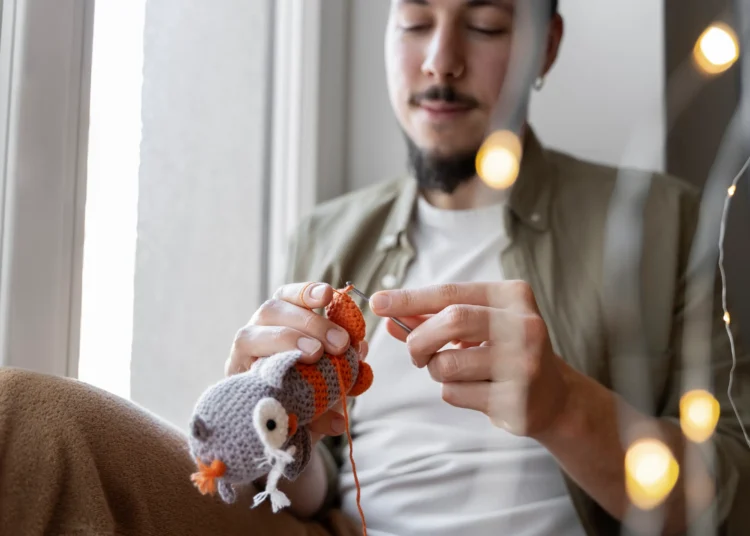 Homem crocheting um brinquedo de crochê com fios coloridos, criando um presente feito à mão com atenção e carinho.