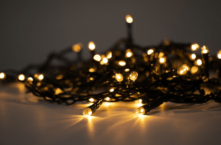 Luzes de Natal amarelas acesas com fios pretos, foco em lâmpadas próximas em superfície branca