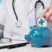 Médico segurando moeda simbólica de saúde enquanto coloca em um cofrinho azul, representando economia e contestação de reajustes de plano de saúde.