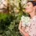Mulher em contato com flores brancas em um jardim, representando o bem-estar emocional proporcionado por plantas que florescem no verão.
