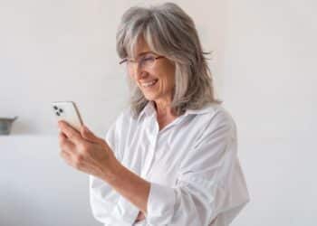 Mulher sorridente e elegante lendo mensagens de boa noite no seu smartphone, em um momento de gratidão e fé antes de dormir.