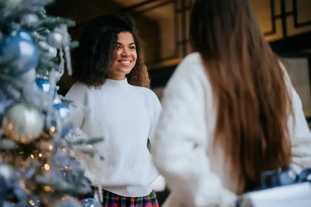 Duas pessoas sorrindo e se encontrando ao redor de uma árvore de Natal, representando momentos de conexão e cuidado emocional durante o fim de ano.
