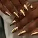 Unhas com esmalte cromado dourado e anéis dourados em destaque.