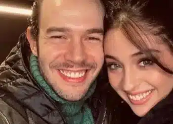 Selfie em close dos atores turcos Aytaç Şaşmaz e Cemre Baysel sorrindo e encostando os rostos. Aytaç usa uma jaqueta preta com gola alta de lã verde e Cemre veste uma blusa preta de gola alta.