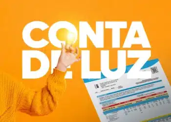 Pessoa de suéter laranja segura lâmpada acesa ao lado de conta de energia elétrica.