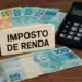 Dinheiro, calculadora e placa de Imposto de Renda sobre a mesa.
