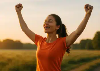Mulher sorridente com braços erguidos ao ar livre ao pôr do sol