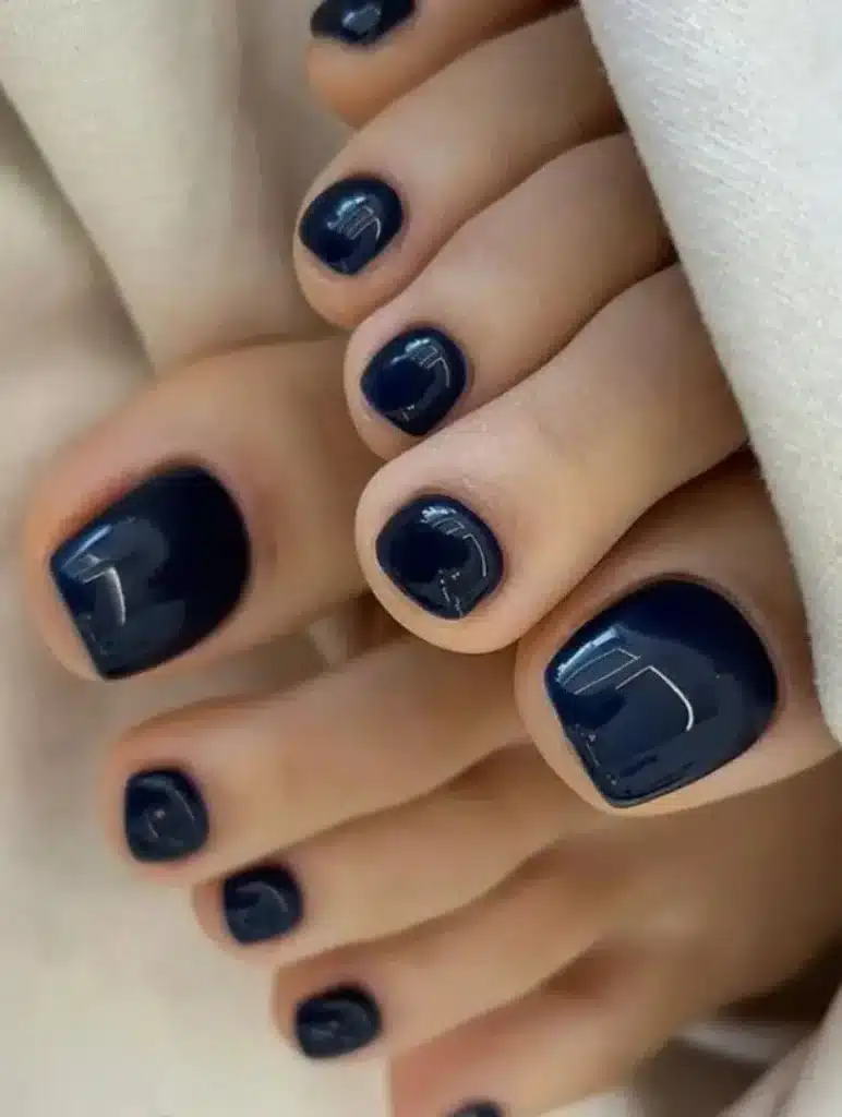 Unhas dos pés esmaltadas em azul escuro com acabamento brilhante e moderno.