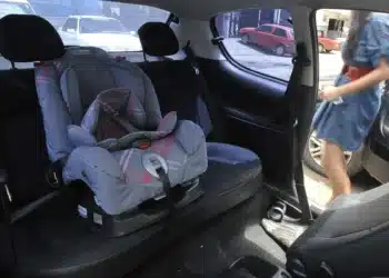 Cadeirinha de bebê instalada no banco traseiro de um carro, com assento acolchoado e cinto de segurança visível.