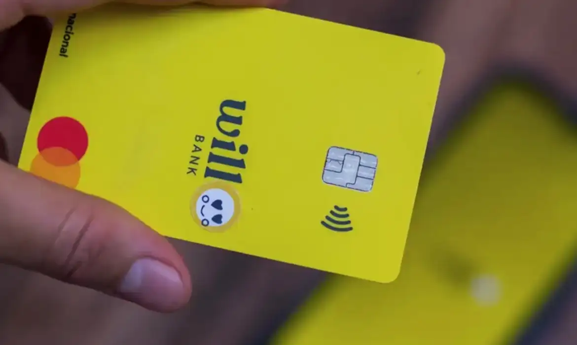 Mão segurando cartão Will Bank amarelo com tecnologia contactless