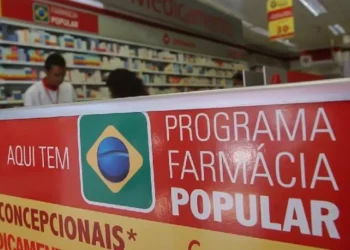 Cartaz do Programa Farmácia Popular em farmácia com prateleiras e atendentes ao fundo